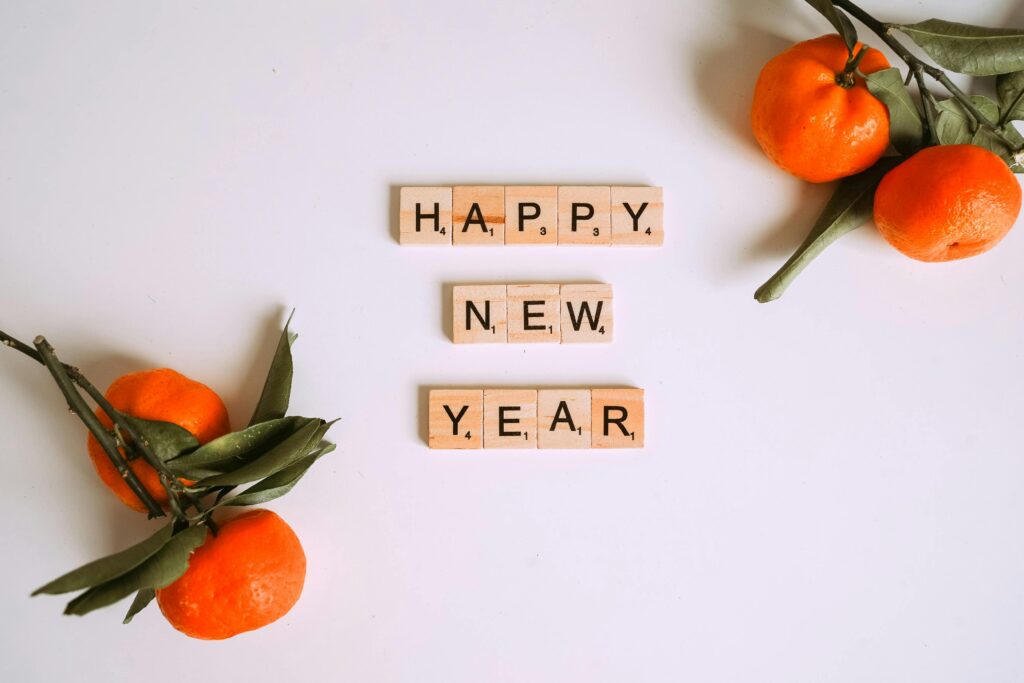 Happy New Year message with Scrabble tiles and fresh mandarins for festive decor.